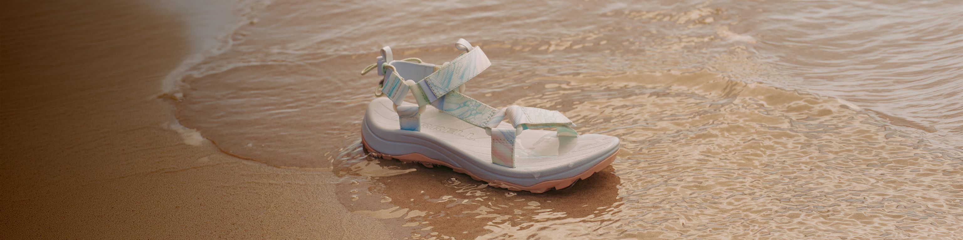 A Merrell sandal in shallow water on the beach.